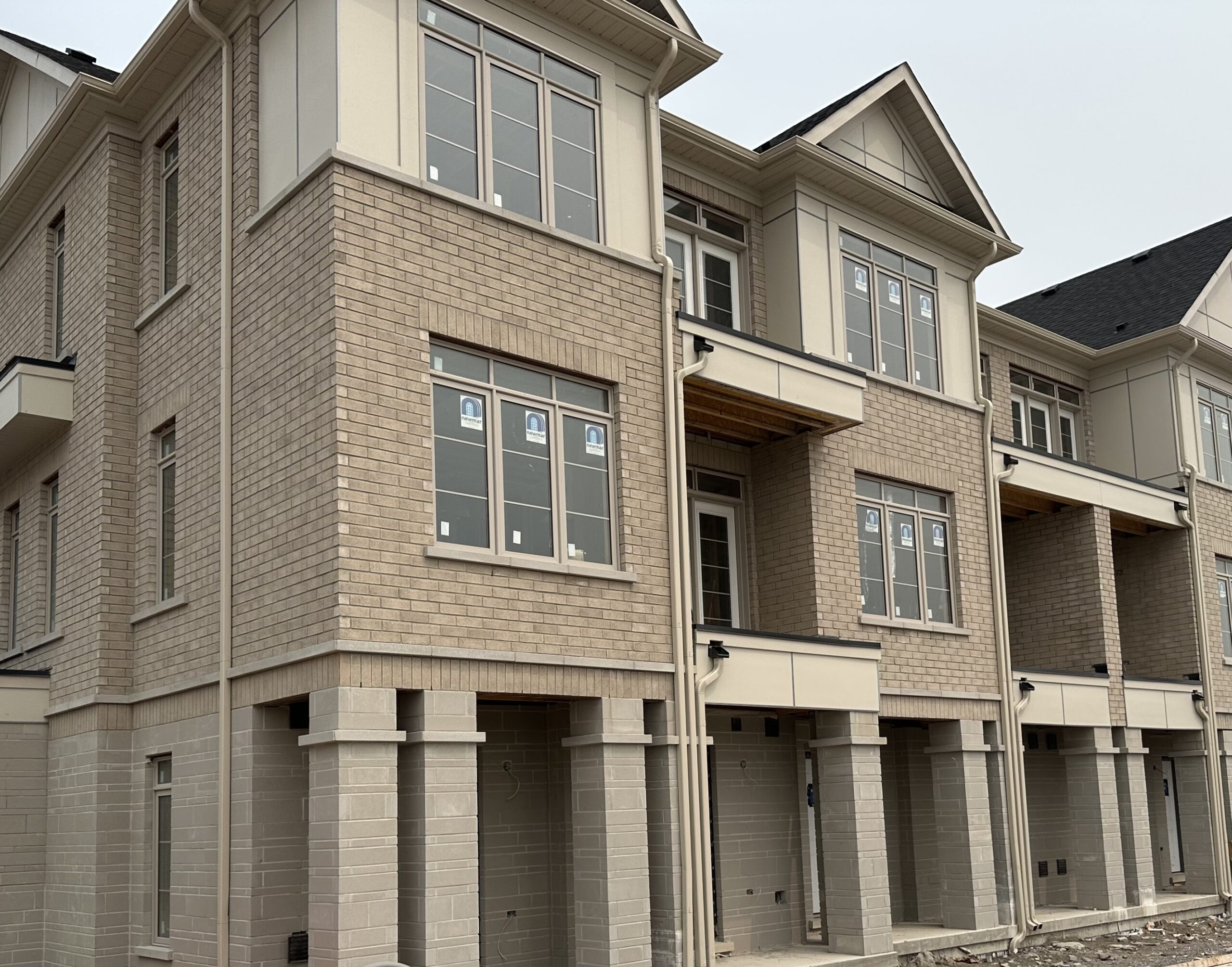 A row of two-story townhouses with brick facades and small front yards, lined up along a quiet street